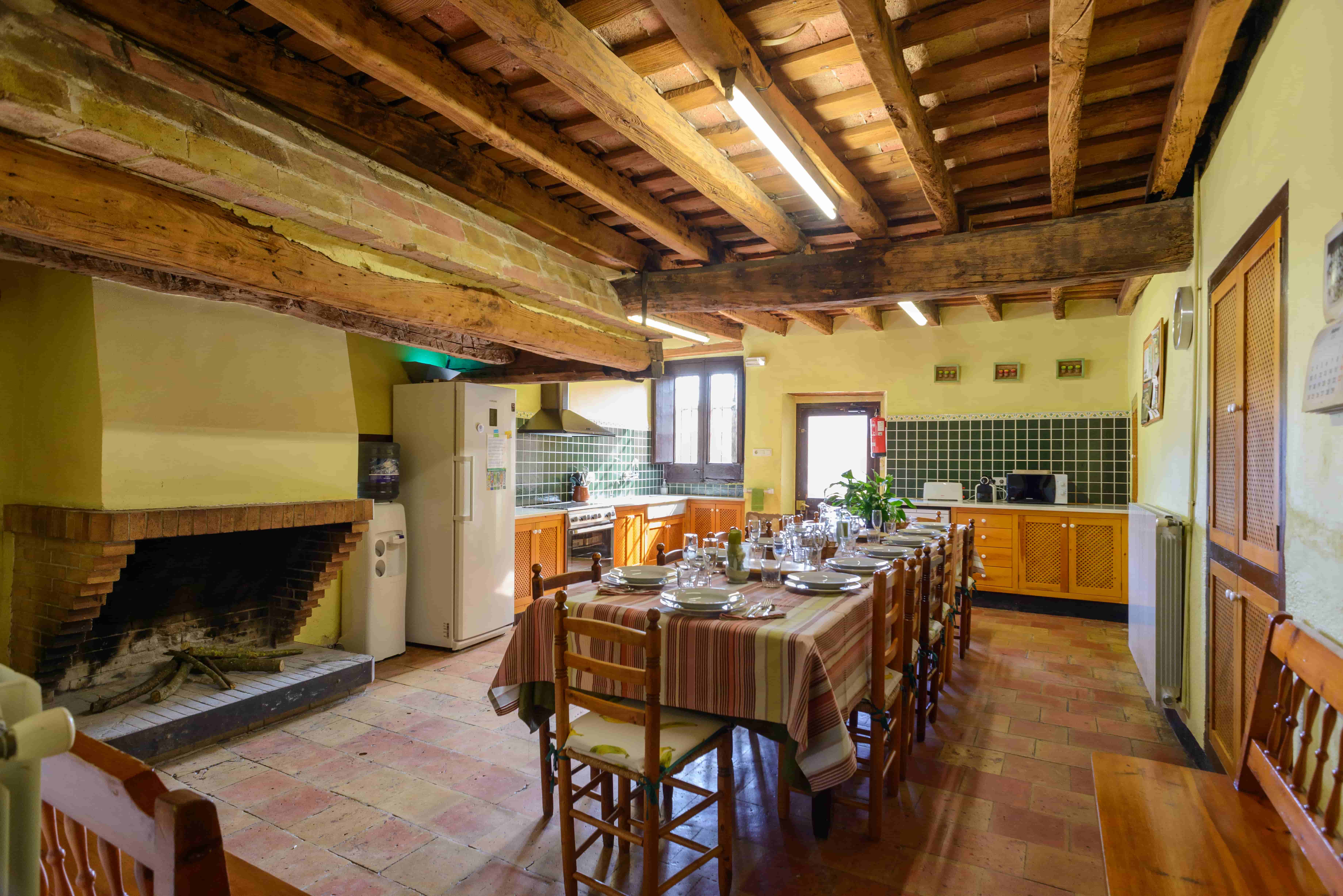 Cocina grande con la mesa preparada, con una chimenea grande a la izquierda con madera preparada para encender el fuego.